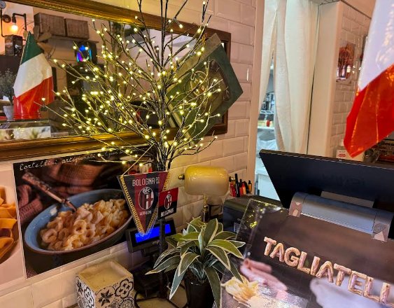 Specchio dorato con riflesso pasta, bandiere italiane e albero LED — dettagli magici del locale Bologna